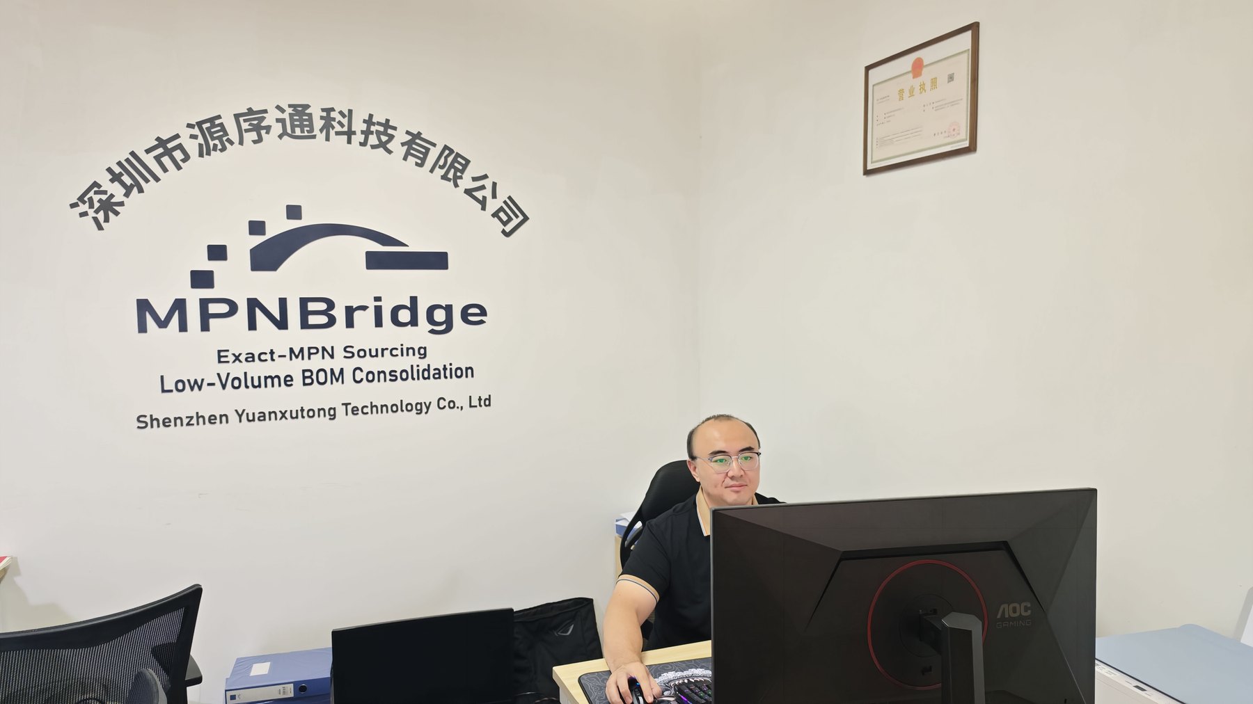Jason Cheng working at the MPNBridge office in Bao'an District, Shenzhen, in front of the company sign wall.